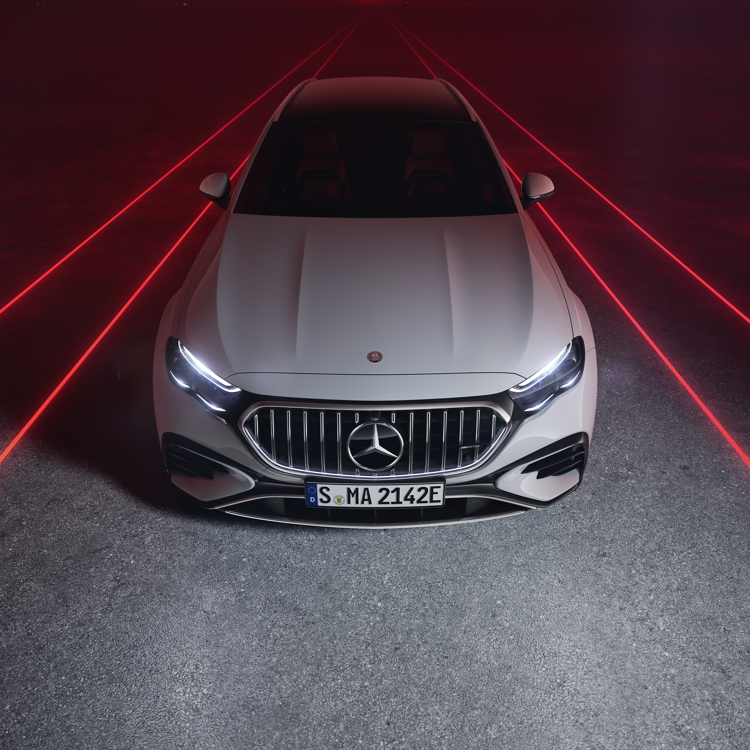 Mercedes-AMG E 53 HYBRID 4MATIC+ pri pohľade spredu zhora pred červeným pozadím.