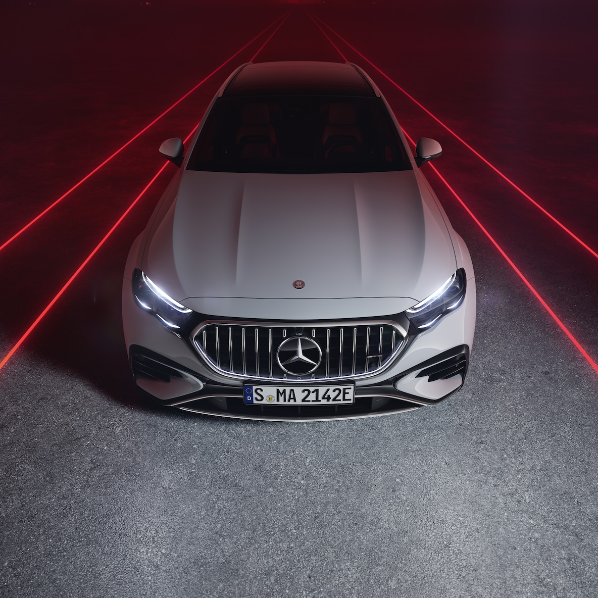Mercedes-AMG E 53 HYBRID 4MATIC+ pri pohľade spredu zhora pred červeným pozadím.