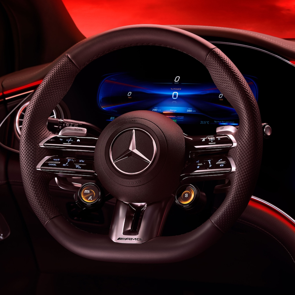 Pohľad na volant AMG Performance zo sedadla vodiča pred červeným pozadím.