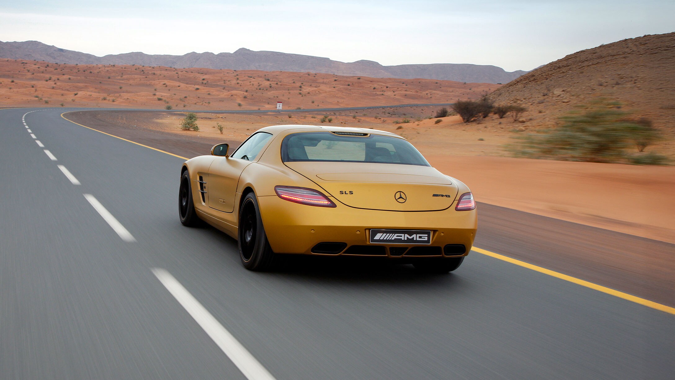 Oranžový SLS AMG ide po prázdnej ceste polopúštnou krajinou.