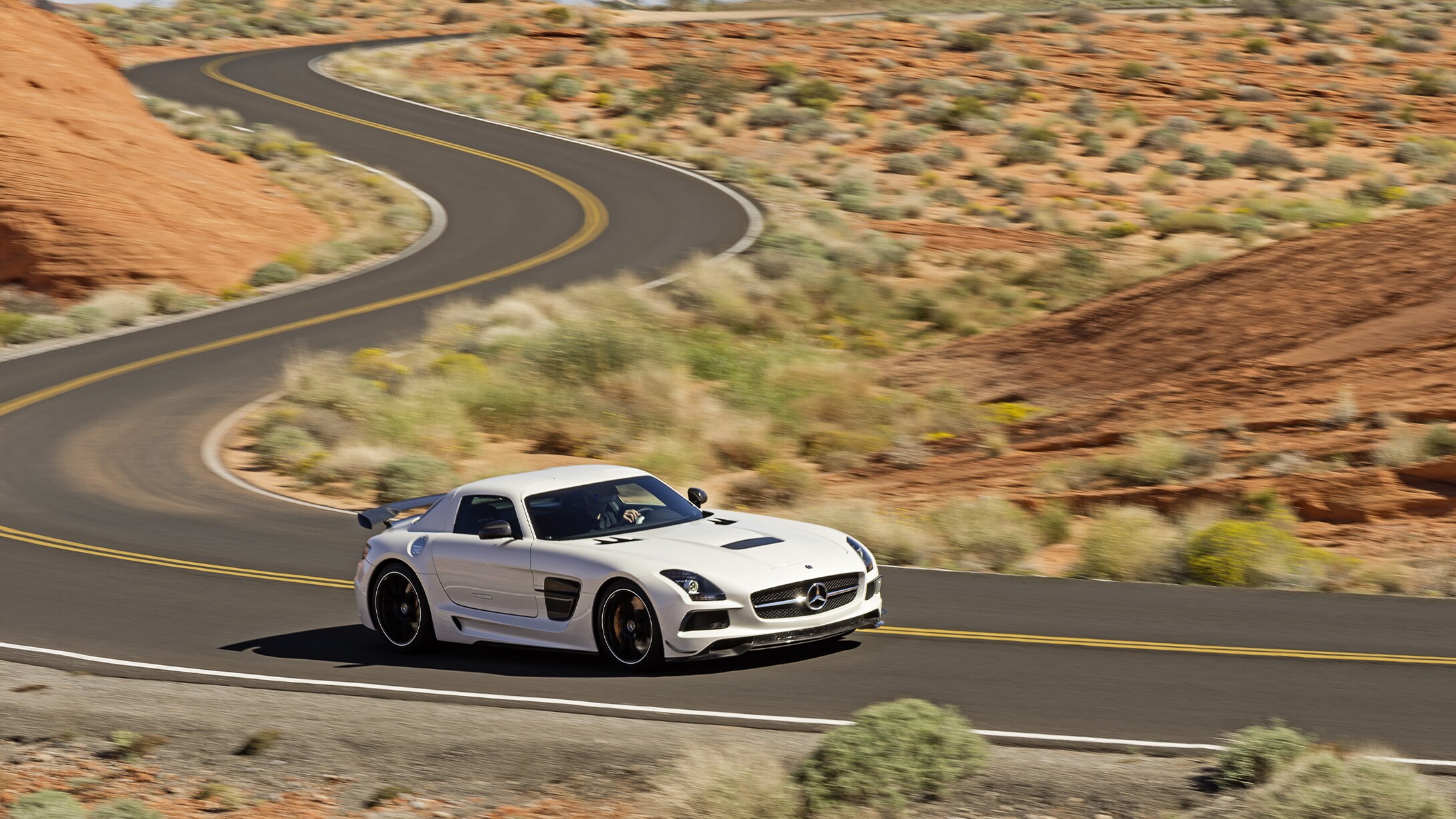 Biely SLS AMG Black Series ide po prázdnej ceste polopúštnou krajinou.