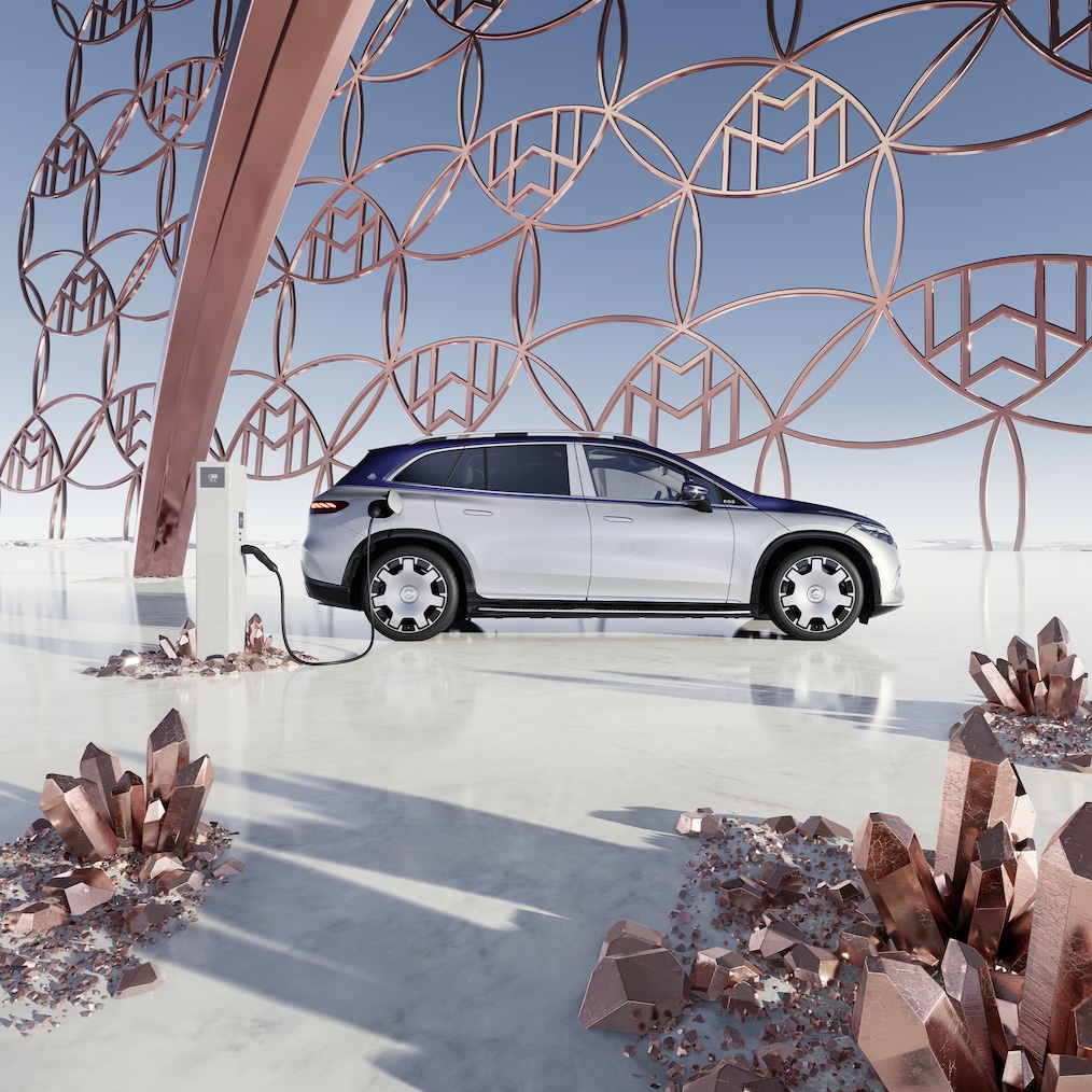 Pohľad zboku na Mercedes-Maybach EQS SUV na nabíjacej stanici s logom značky Maybach brand logo v pozadí.