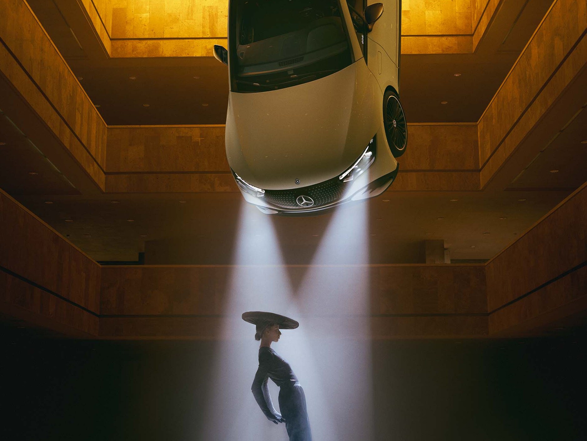 Tmavý priestor so svetlometmi zavesenými na strope, pričom v&nbsp;ich svetelnom kuželi stojí žena.