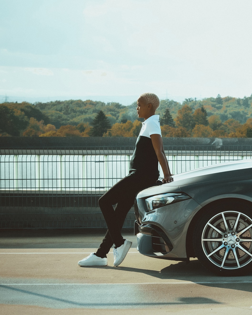 Kolekcia Mercedes-Benz AMG | Mercedes-Benz Mladá žena v outfite z kolekcie AMG Racing sa nedbalo opiera o kapotu motora vozidla Mercedes.