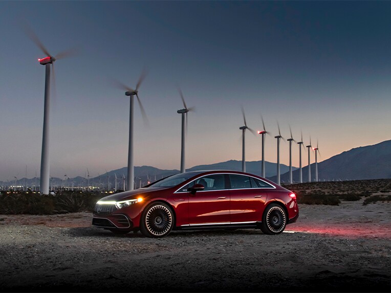 Červená EQS od značky Mercedes-Benz (V 297) zaparkovaná pred veterným kolesom.