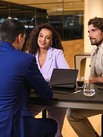 Traja ľudia sediaci na stole sa zapájajú v diskusii.