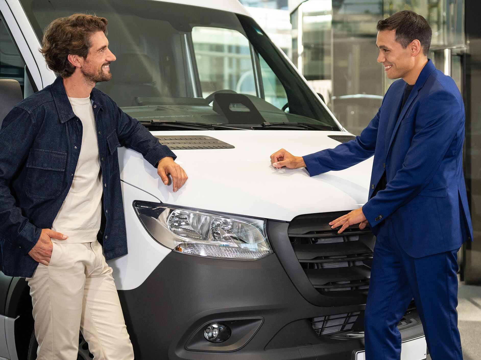 Dvaja ľudia, ktorí sa opierajú o dodávku Mercedes-Benz a majú rozhovor.