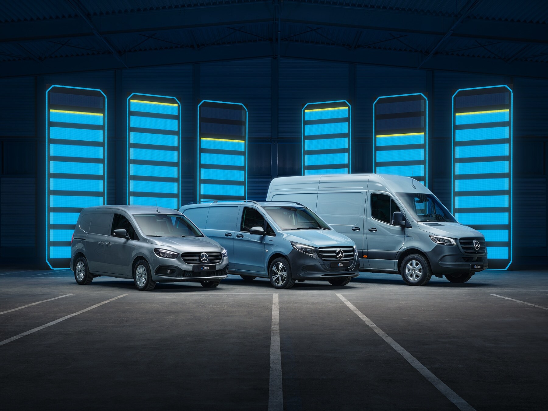 Modelový rad elektrických transportérov Mercedes-Benz vystavený vo futuristickom sklade s&nbsp;osvetlenými nabíjacími lištami
