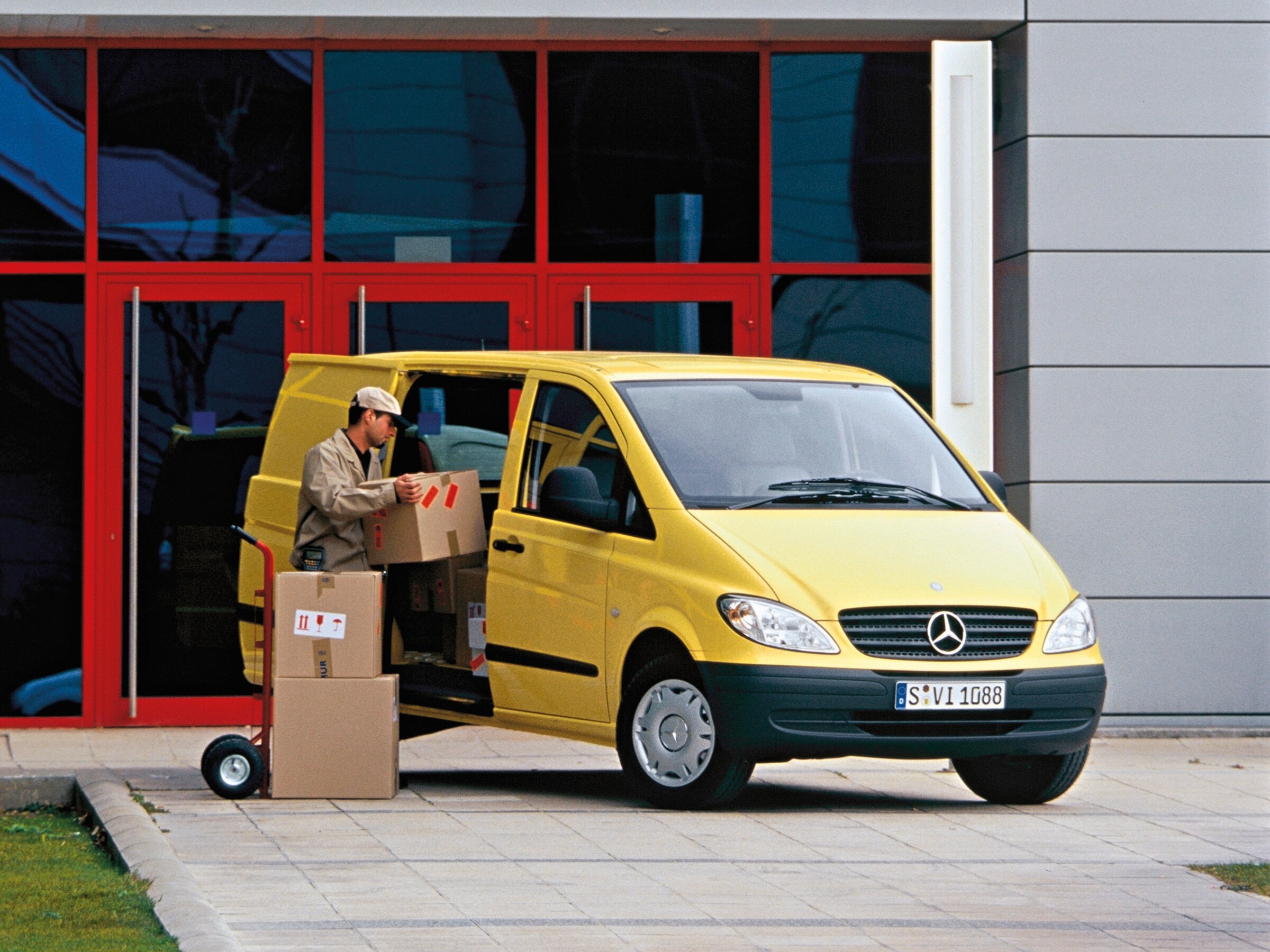 Žlté vozidlo Mercedes-Benz Vito zaparkované pred budovou s&nbsp;pracovníkom vykladajúcim balíky
