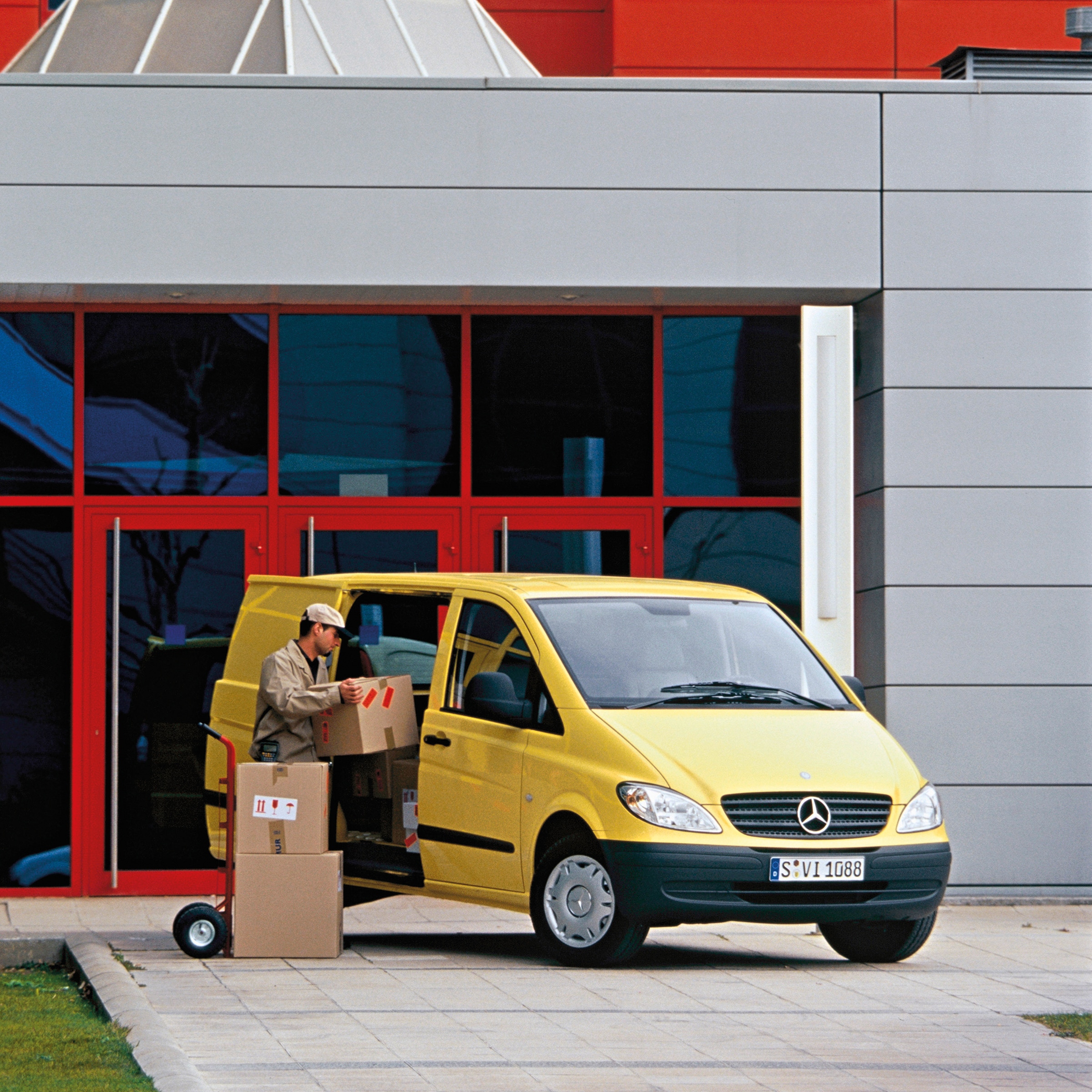 Druhá generácia vozidiel Mercedes-Benz Vito | História úžitkových vozidiel | Mercedes-Benz Žlté vozidlo Mercedes-Benz Vito zaparkované pred budovou s pracovníkom vykladajúcim balíky