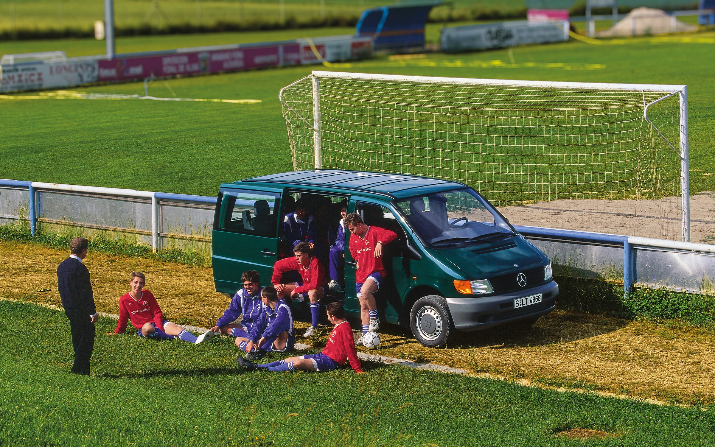 Prvá generácia vozidiel Mercedes-Benz Vito | História úžitkových vozidiel | Mercedes-Benz Vito prvej generácie zaparkované vedľa futbalového ihriska s hráčmi tímu v blízkosti