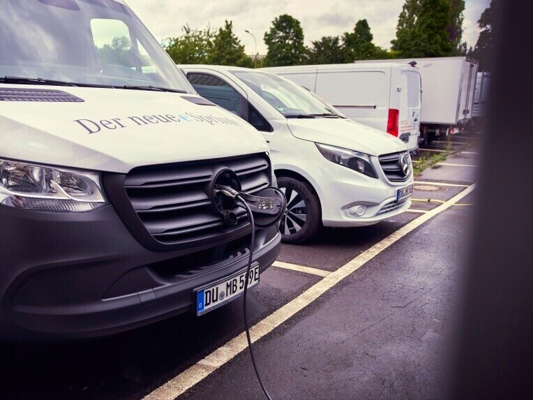 eSprinter, elektrický transportér od Mercedes-Benz, je počas nabíjania pripojený na nabíjacej stanici. V pozadí stoja ďalšie elektrické transportéry.