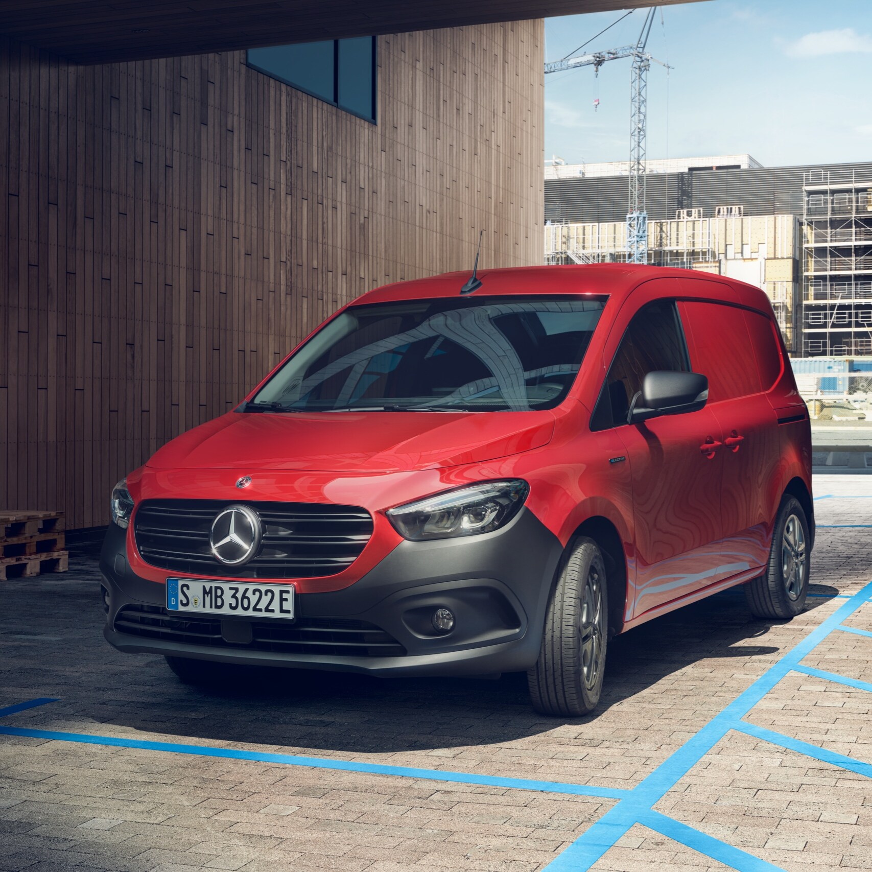 Skriňové vozidlo eCitan, elektrický transportér od značky Mercedes-Benz, parkuje pri nabíjacom stojane pred modernou budovou.