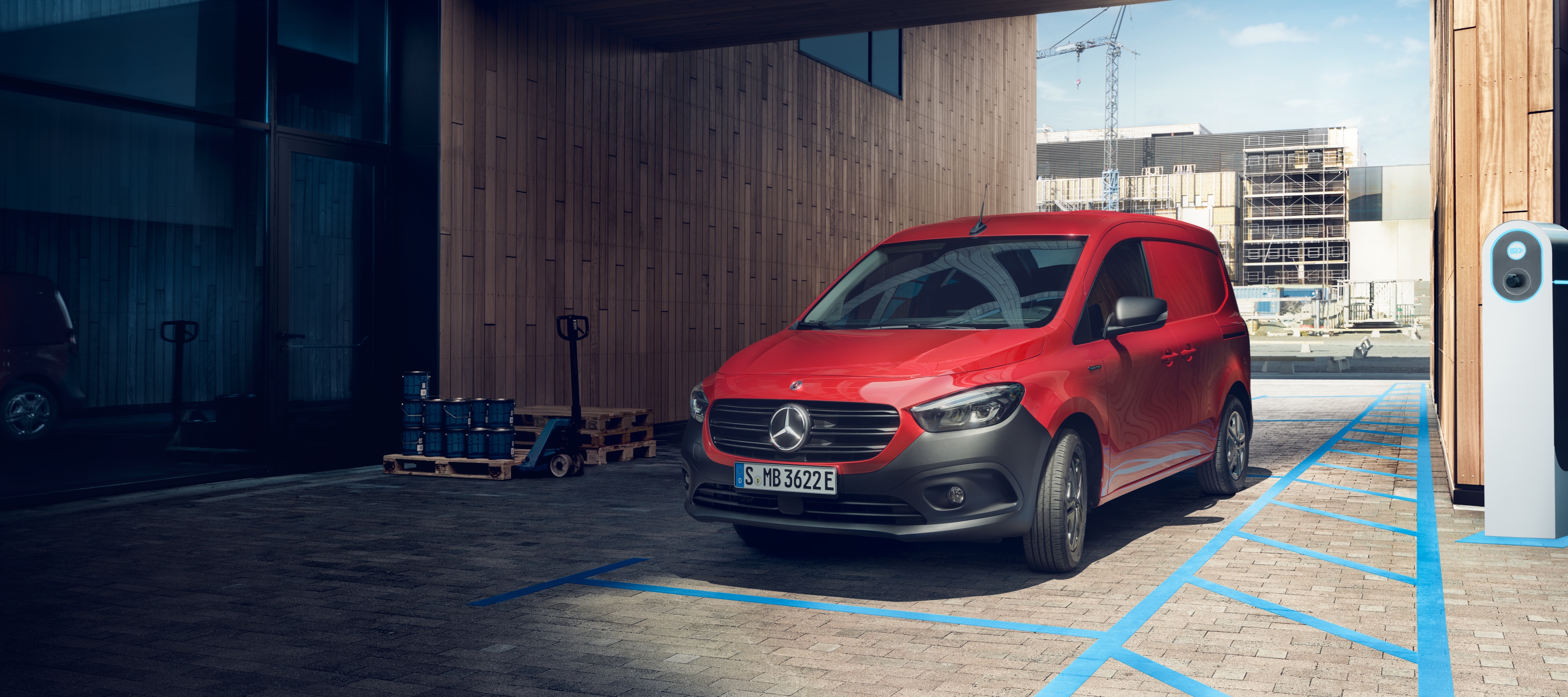 Skriňové vozidlo eCitan | Transportéry Mercedes-Benz Skriňové vozidlo eCitan, elektrický transportér od značky Mercedes-Benz, parkuje pri nabíjacom stojane pred modernou budovou.