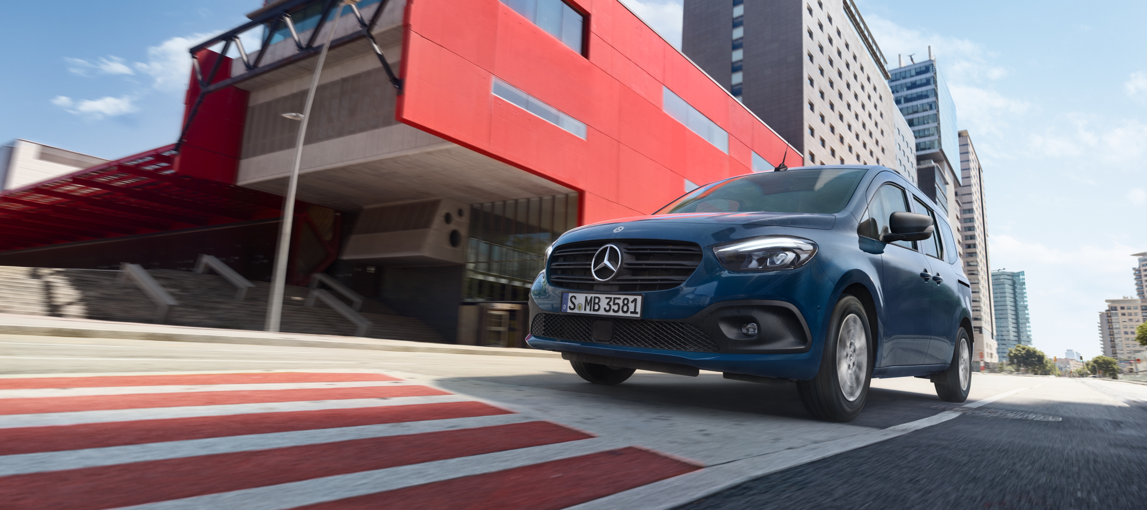 eCitan Tourer | Transportéry Mercedes-Benz eCitan Tourer, elektrický transportér na prepravu osôb od značky Mercedes-Benz, počas jazdy cez modernú mestskú oblasť.