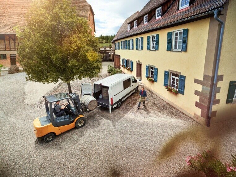 Vidlicový nakladač nakladá na dvore ťažký predmet do skriňového vozidla Mercedes-Benz Sprinter.