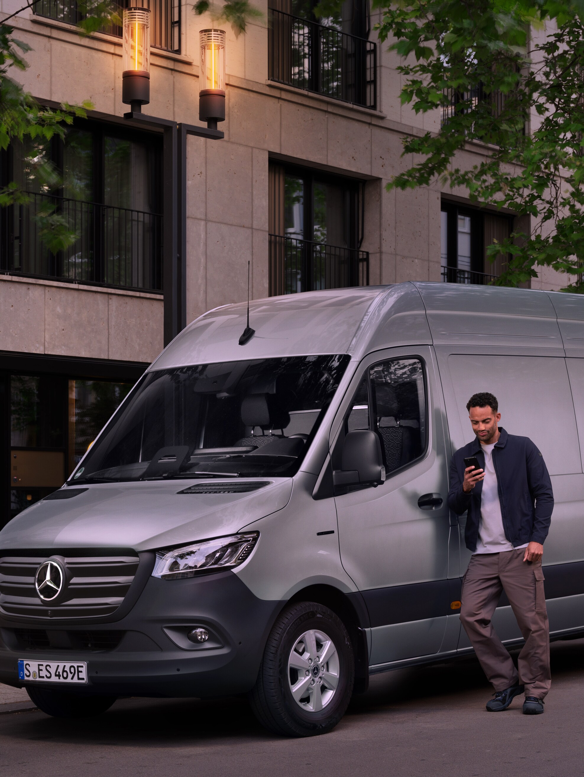Muž sa opiera o strieborné úžitkové vozidlo Mercedes-Benz Sprinter a používa svoj chytrý telefón – rýchla pomoc Centra starostlivosti o zákazníkov Mercedes-Benz.