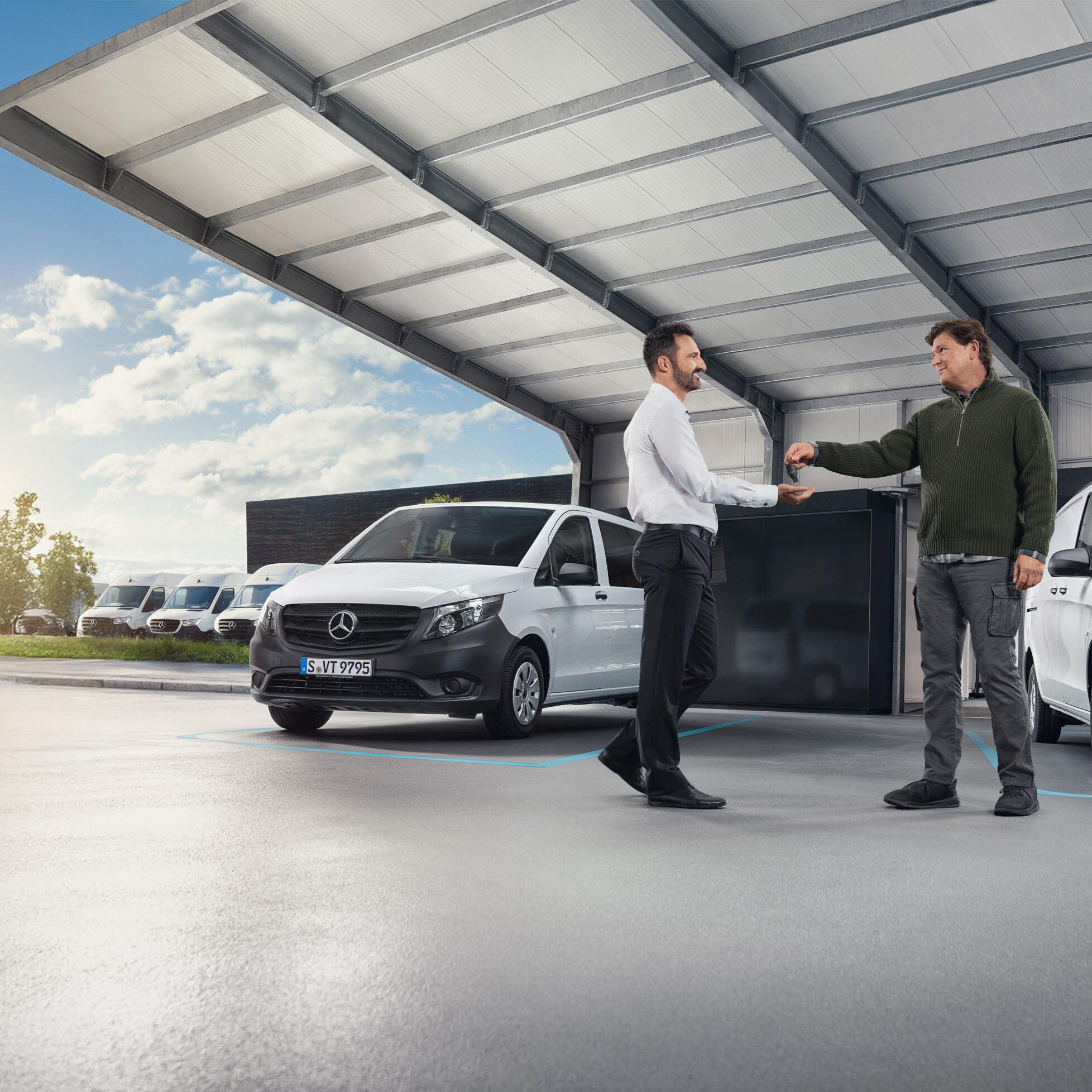 Dvaja muži diskutujú pred radom bielych úžitkových vozidiel Mercedes-Benz v hale.