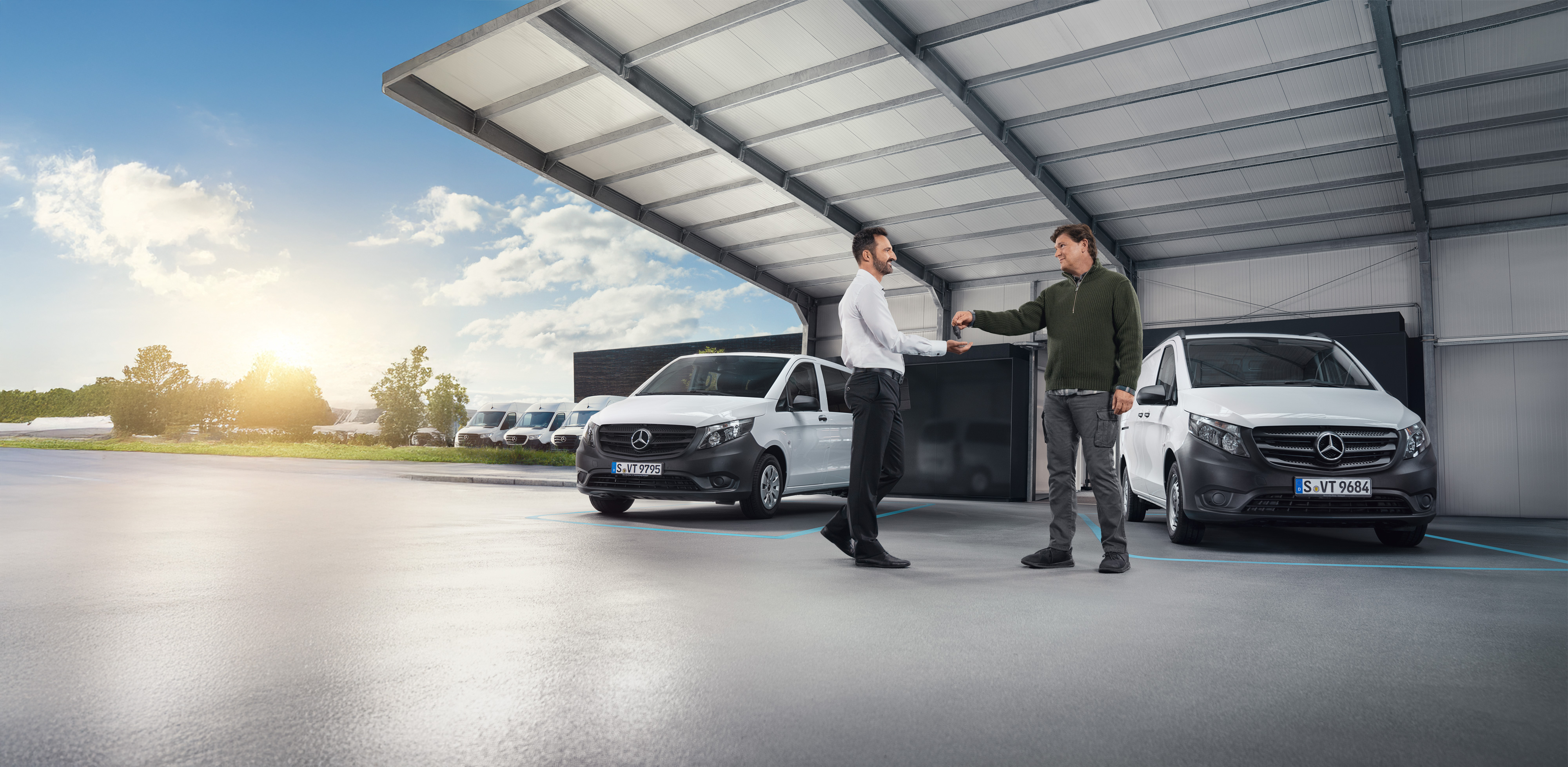 Mercedes-Benz | Starostlivosť o úžitkové vozidlá | Individuálna podpora Dvaja muži diskutujú pred radom bielych úžitkových vozidiel Mercedes-Benz v hale.