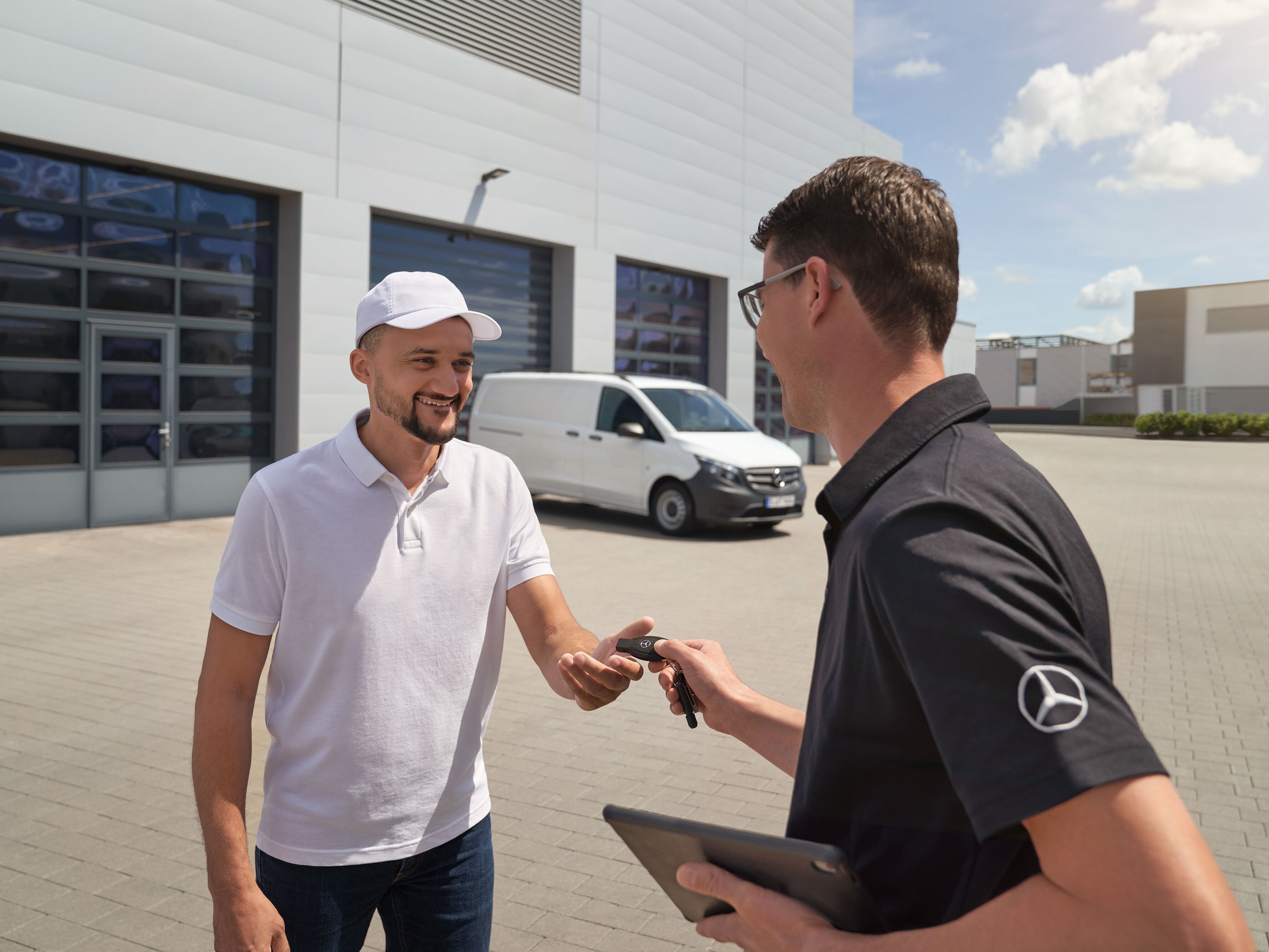 Technik Mercedes-Benz odovzdáva zákazníkovi kľúče, v pozadí je biele úžitkové vozidlo Mercedes-Benz Vito.