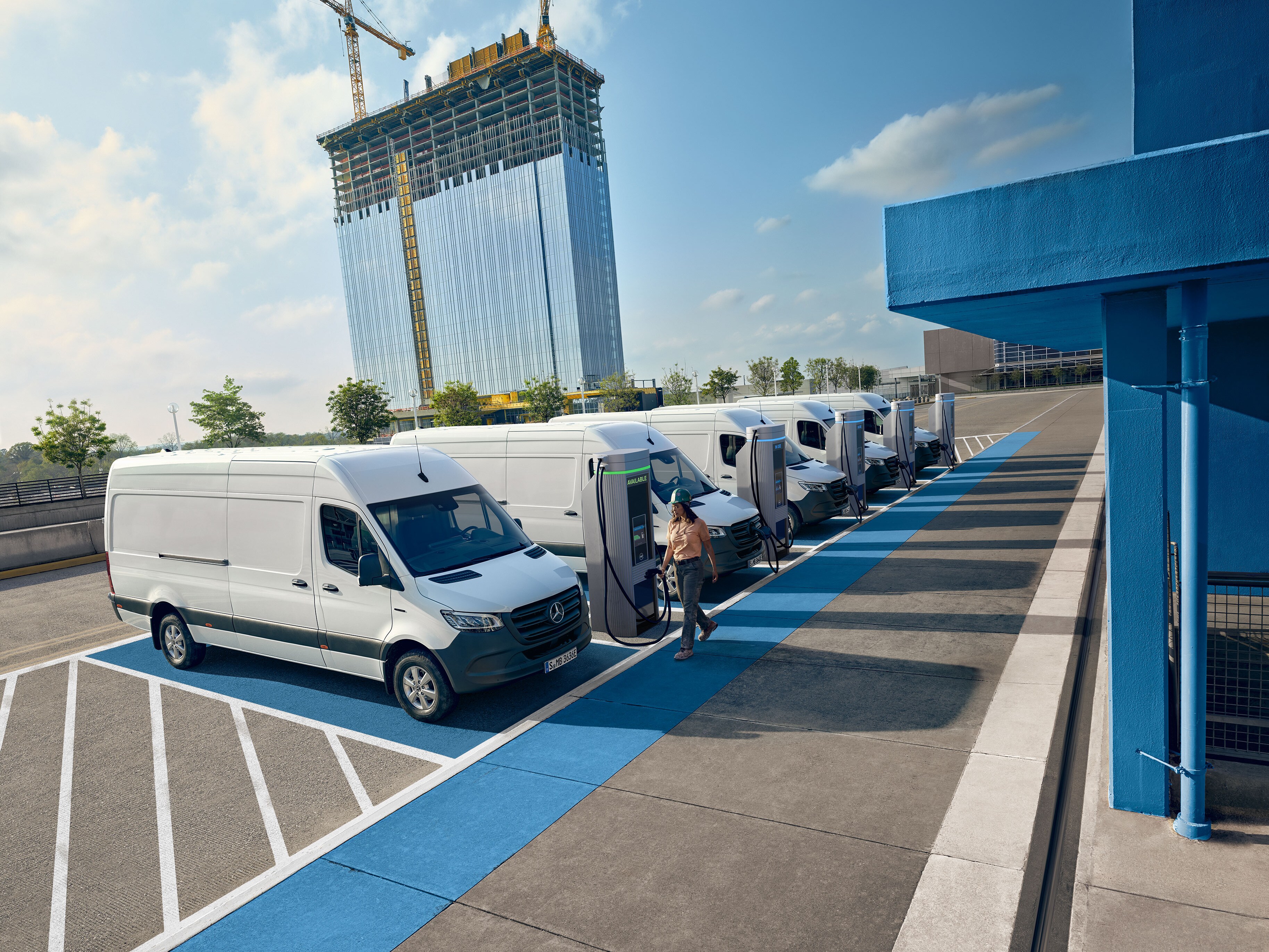 Vozový park bielych elektrických transportérov Mercedes-Benz zaparkovaných na stanici nabíjacieho centra.