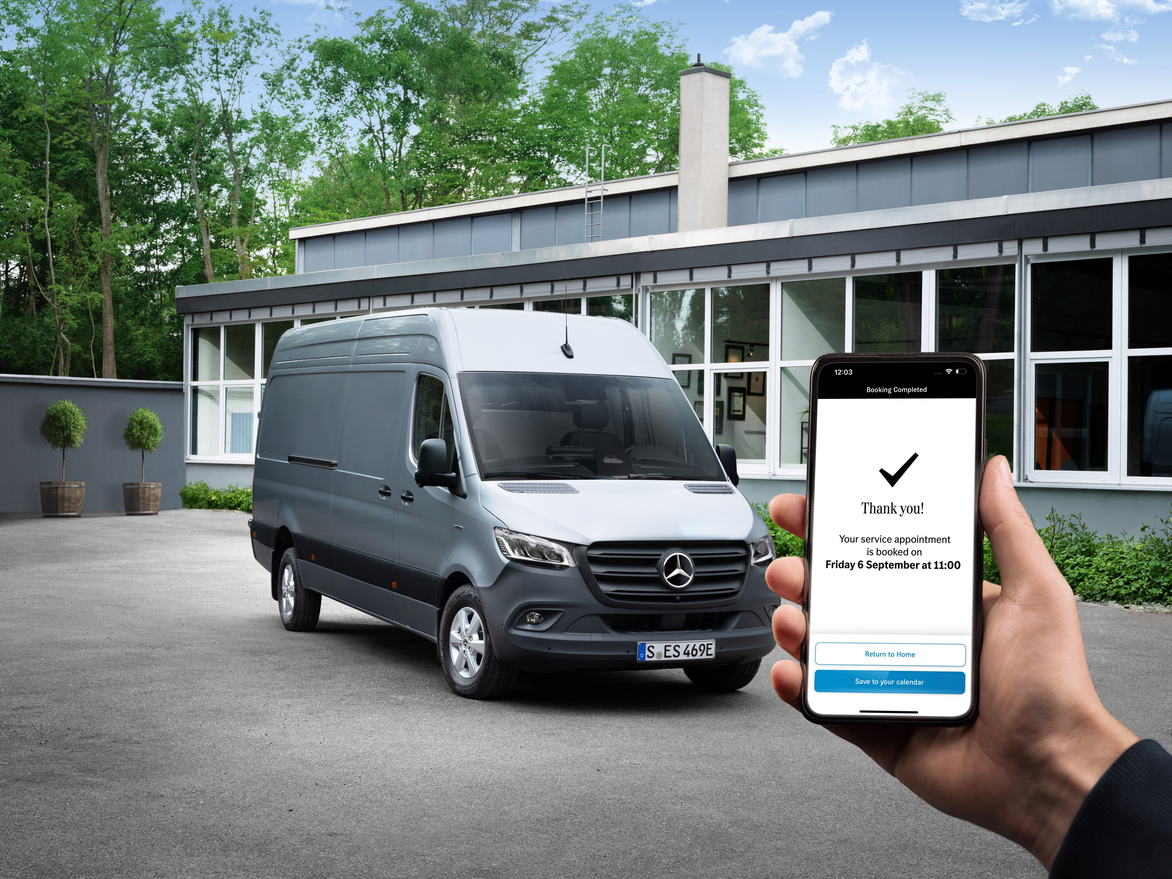 Sivé úžitkové vozidlo Mercedes-Benz Sprinter pred kanceláriou, v popredí osoba s telefónom v ruke.
