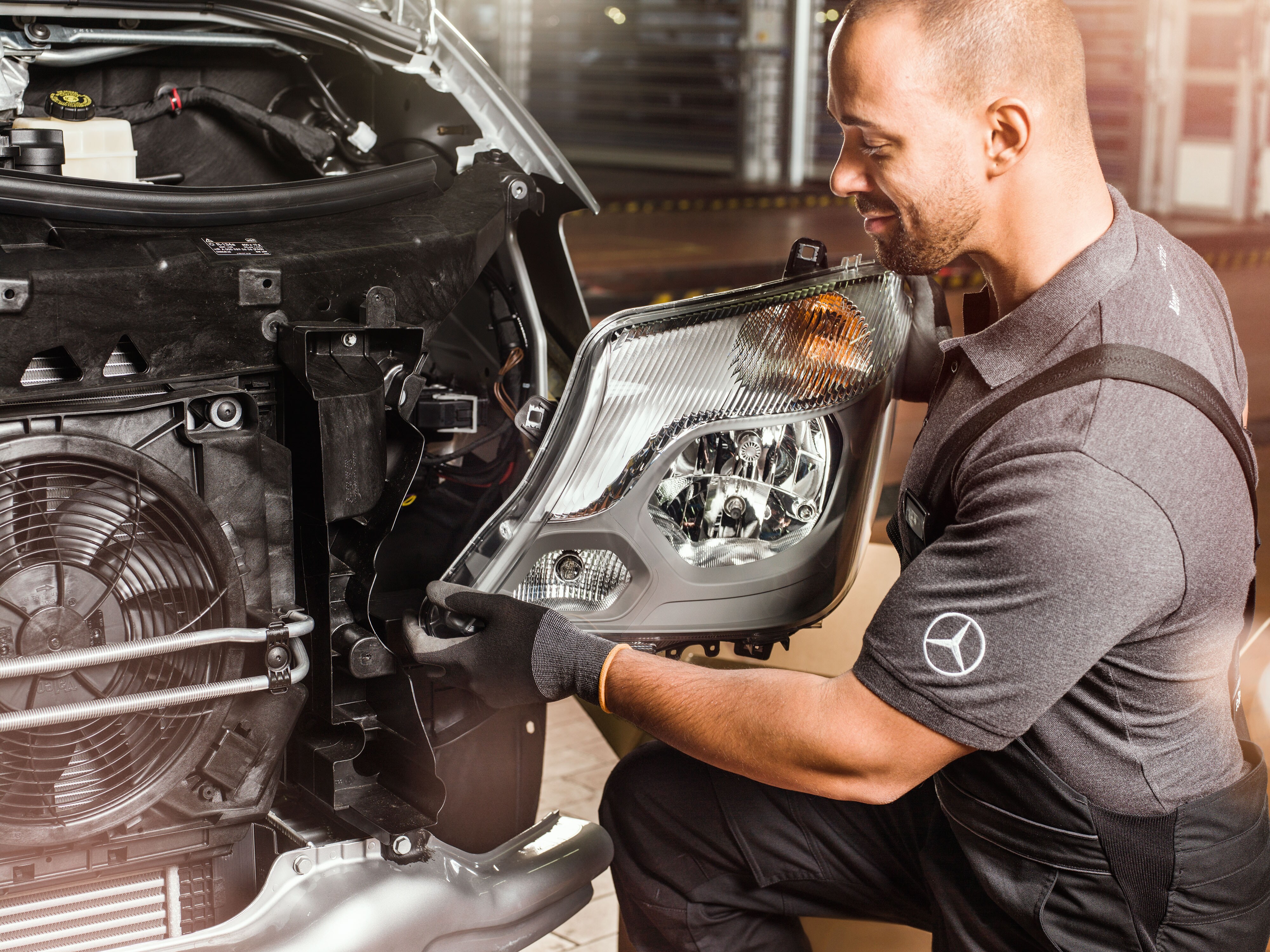 Mechanik kontroluje originálne diely Mercedes-Benz pred otvoreným motorom vozidla Sprinter a&nbsp;porovnáva ich s&nbsp;katalógom náhradných dielov Mercedes.