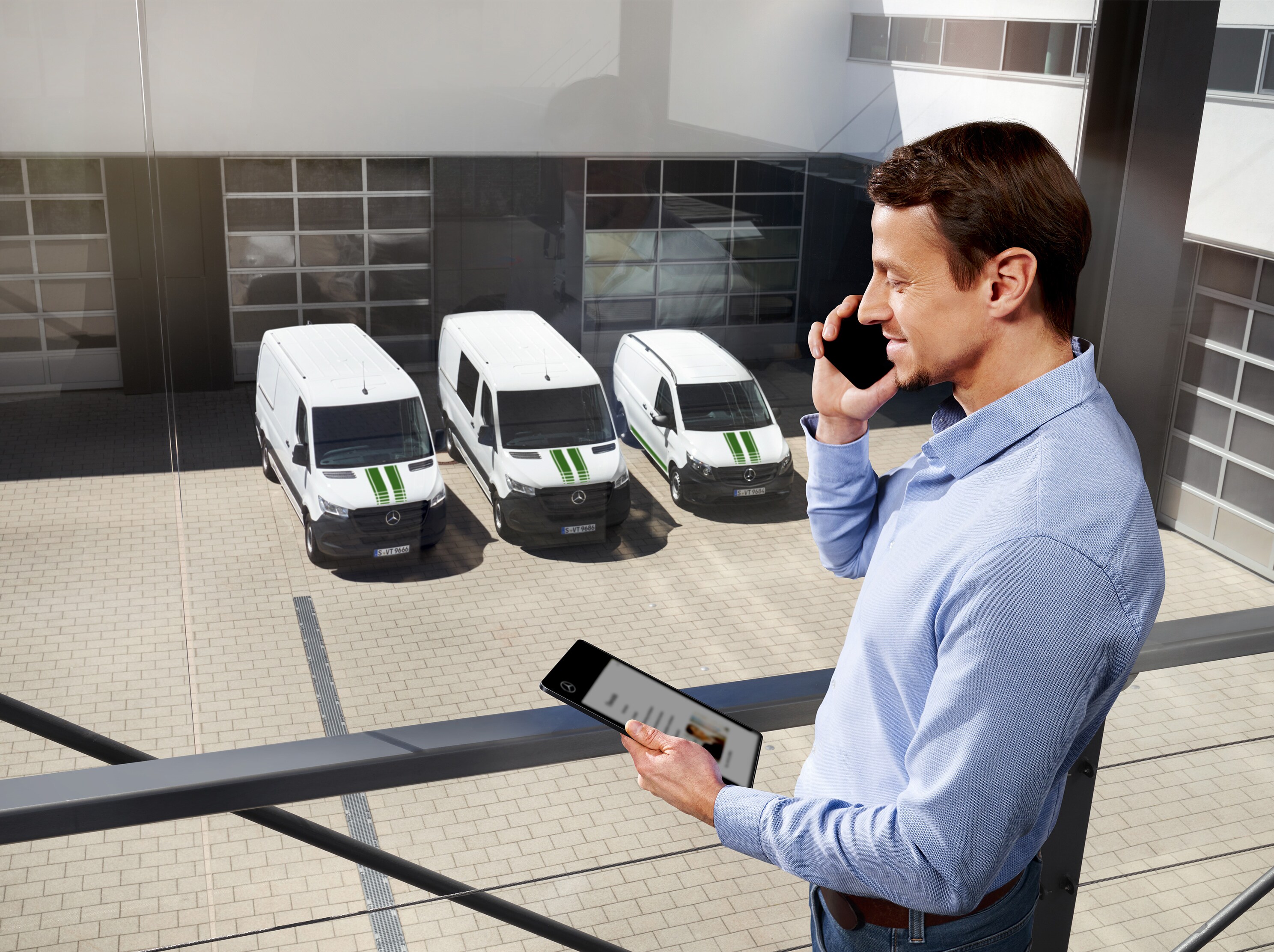 Muž telefonuje s tabletom pred tromi úžitkovými vozidlami Mercedes-Benz, téma: ako dlho trvá záruka výrobcu u Mercedes-Benz?