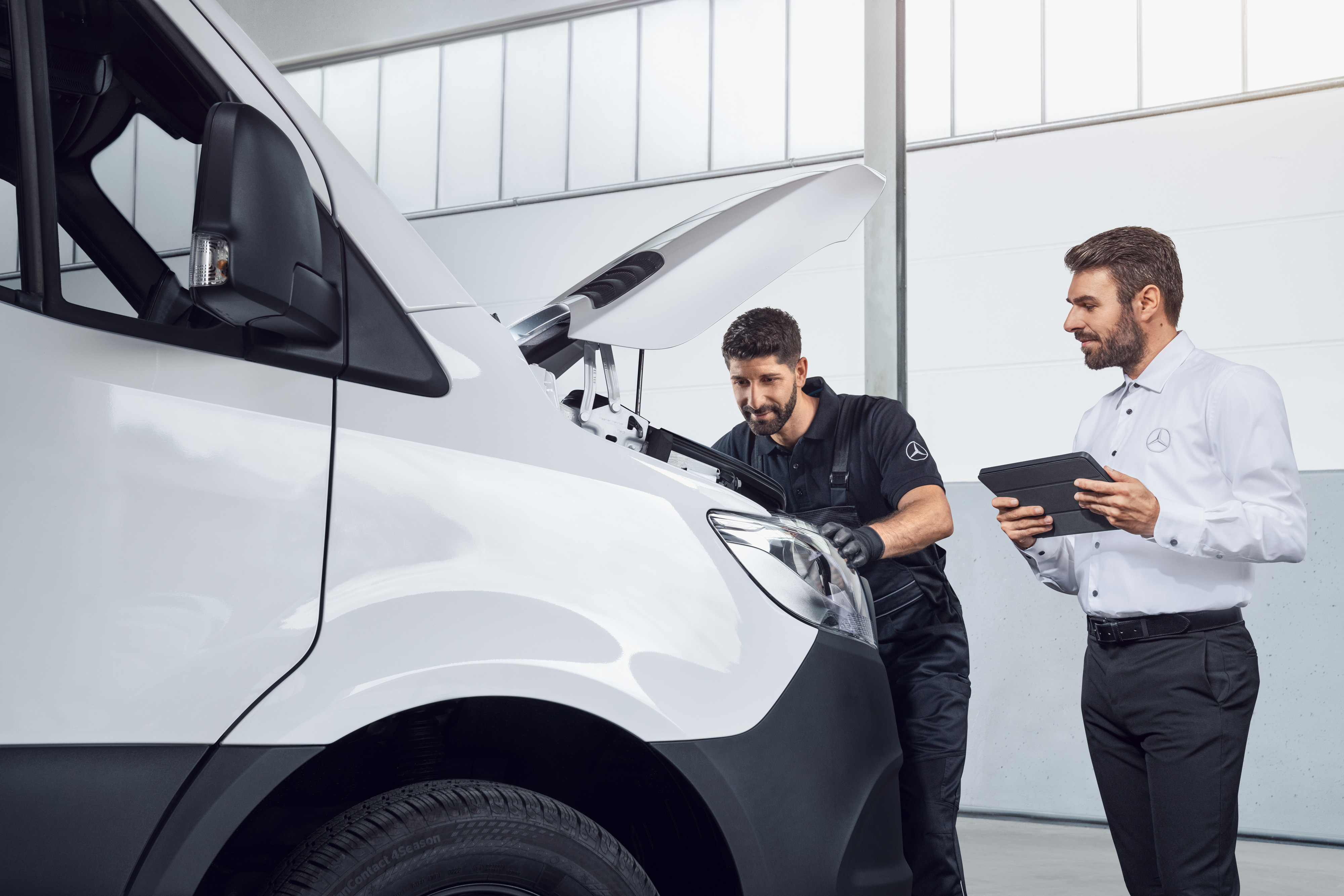 Mercedes-Benz | Kvalita originálnych dielov pre úžitkové vozidlá Dvaja muži testujú vozidlo Mercedes Sprinter s tabletom a otvorenou kapotou motora, téma: náhradné diely pre vozidlo Mercedes-Benz Sprinter.