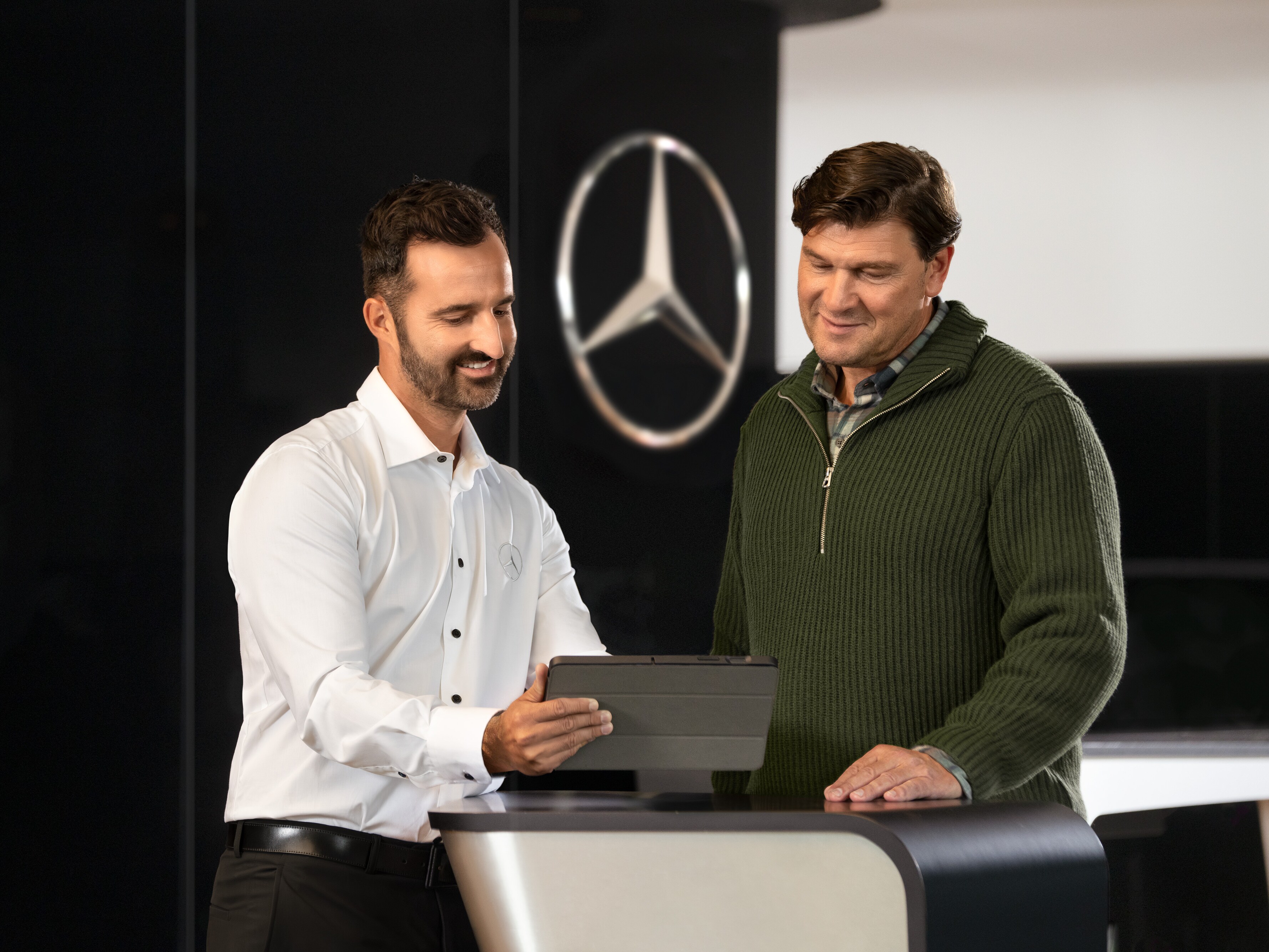 Dvaja muži sa rozprávajú pri pulte a&nbsp;pozerajú sa na tablet pred hviezdou Mercedes-Benz.
