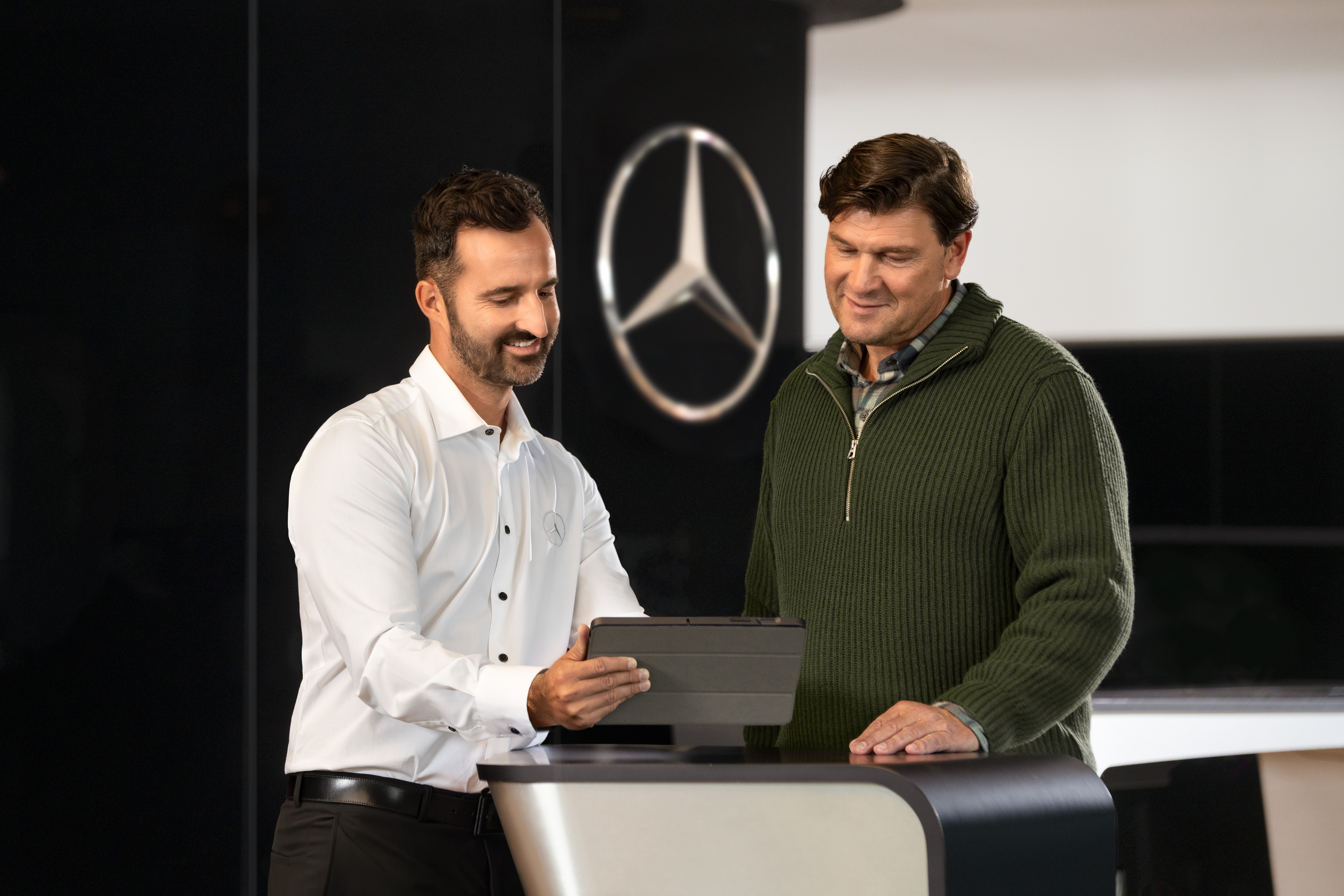 Mercedes-Benz | Prehľad služieb Dvaja muži sa rozprávajú pri pulte a pozerajú sa na tablet pred hviezdou Mercedes-Benz.