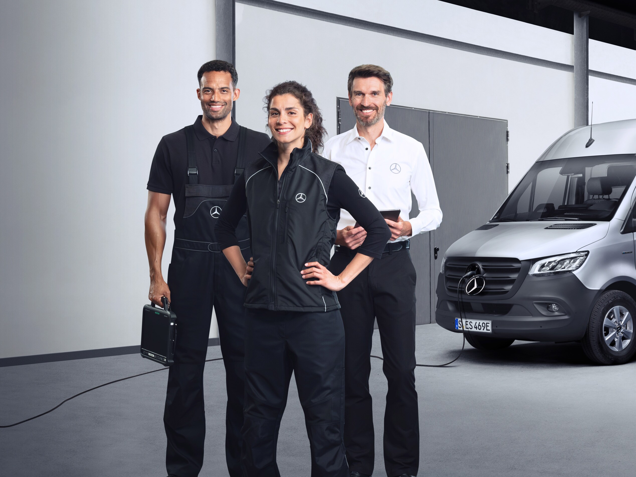 Traja zamestnanci stoja pred strieborným vozidlom Mercedes-Benz eSprinter so zapojeným nabíjacím káblom.