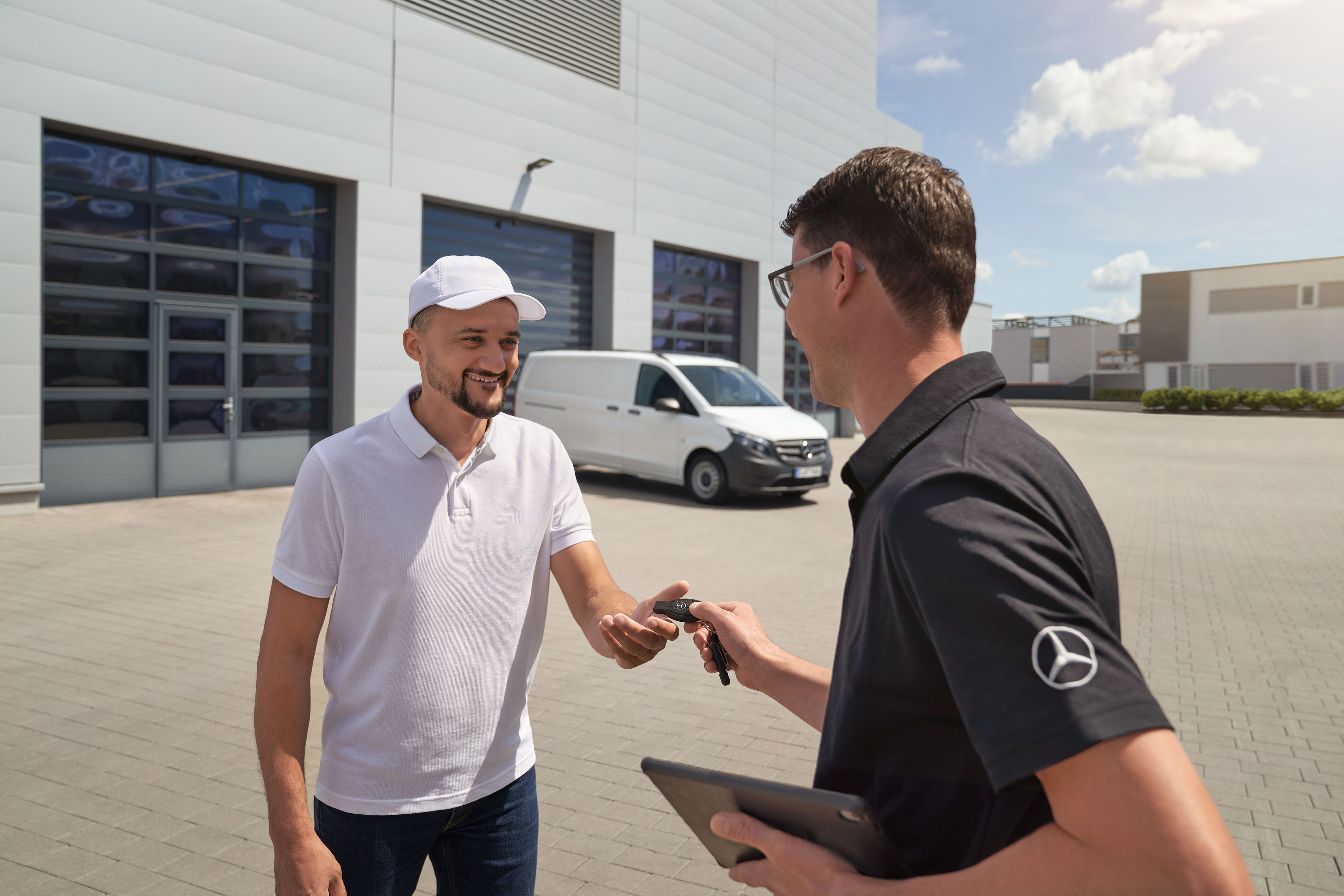 Mercedes-Benz | Údržba | Odvoz a dovoz vozidla Zástupca služieb zákazníkom Mercedes-Benz odovzdáva zákazníkovi kľúče, v pozadí je biele úžitkové vozidlo Mercedes-Benz Vito.