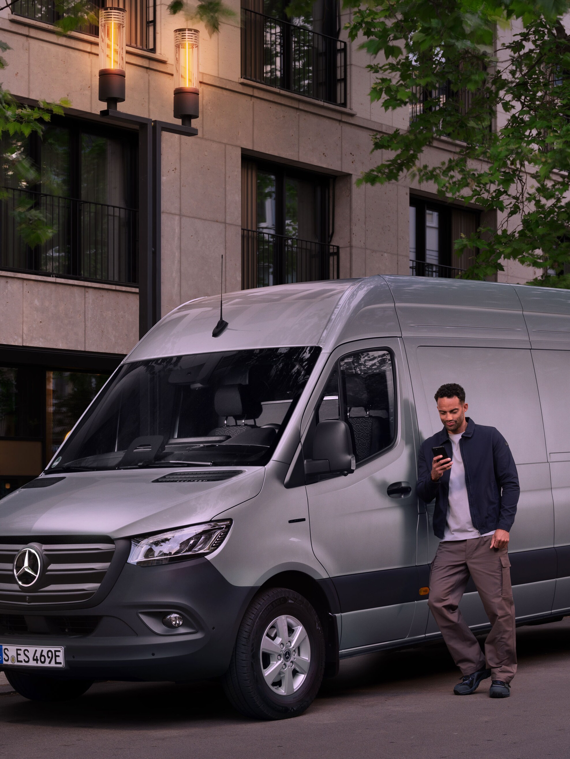 Muž sa opiera o&nbsp;strieborné vozidlo Mercedes-Benz Sprinter a&nbsp;vypĺňa hlásenie o&nbsp;škode vo svojom mobilnom telefóne.