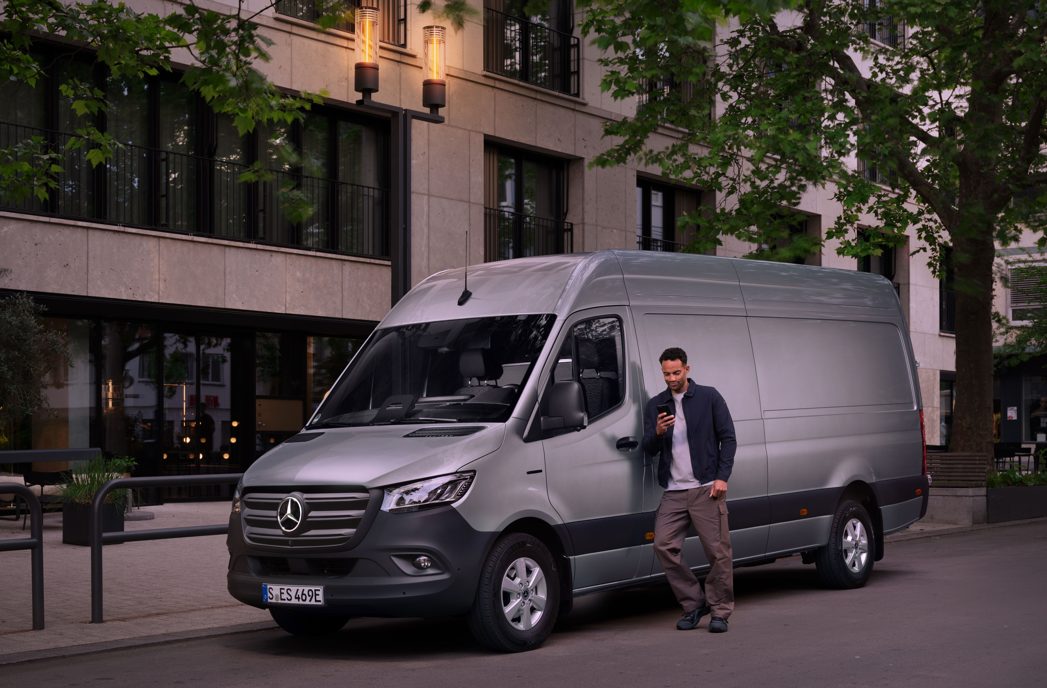 Mercedes-Benz | Oprava | Digitálne hlásenie o škode Muž sa opiera o strieborné vozidlo Mercedes-Benz Sprinter a vypĺňa hlásenie o škode vo svojom mobilnom telefóne.