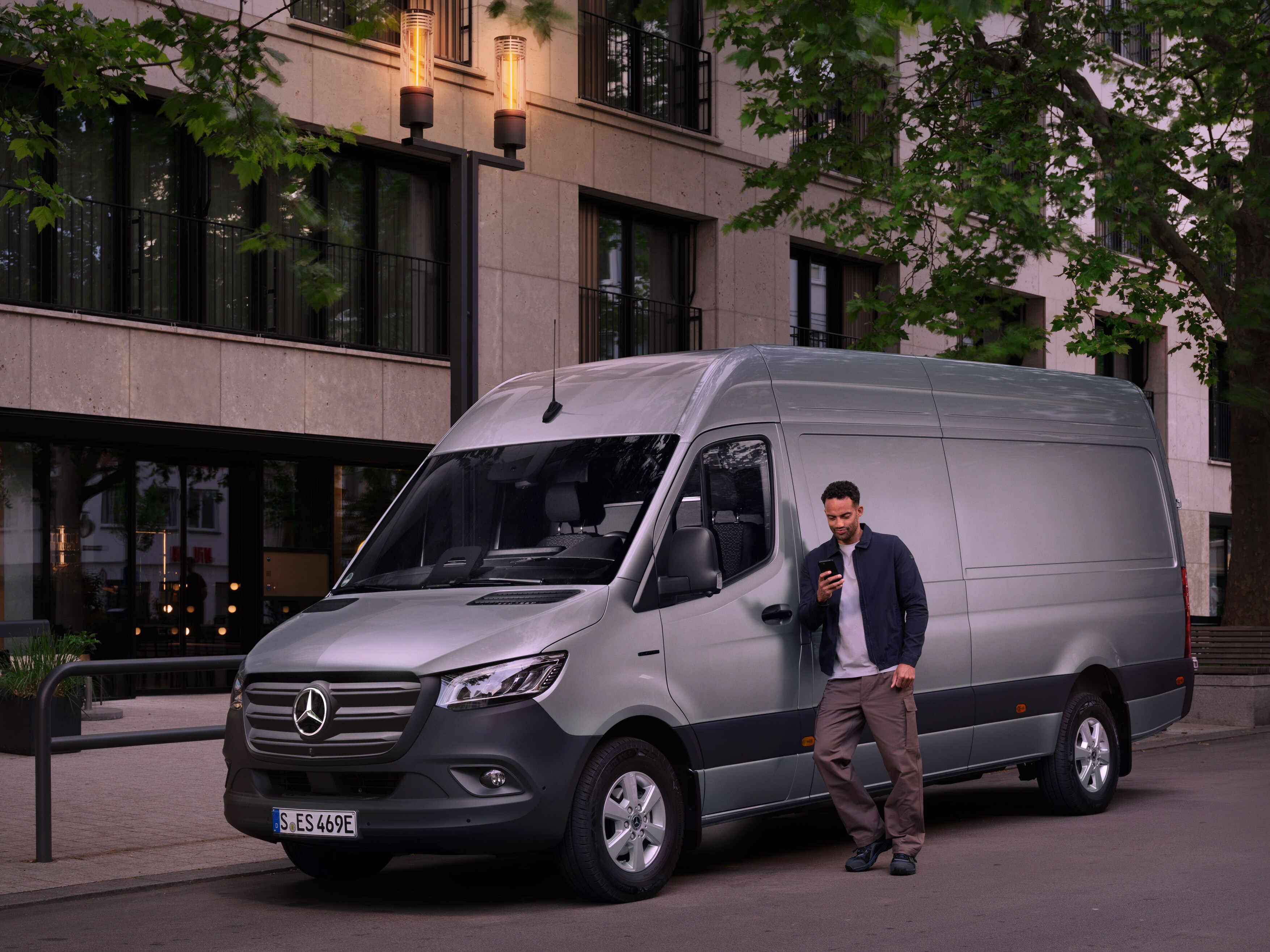 Muž sa opiera o&nbsp;strieborné vozidlo Mercedes-Benz Sprinter a&nbsp;vypĺňa hlásenie o&nbsp;škode vo svojom mobilnom telefóne.