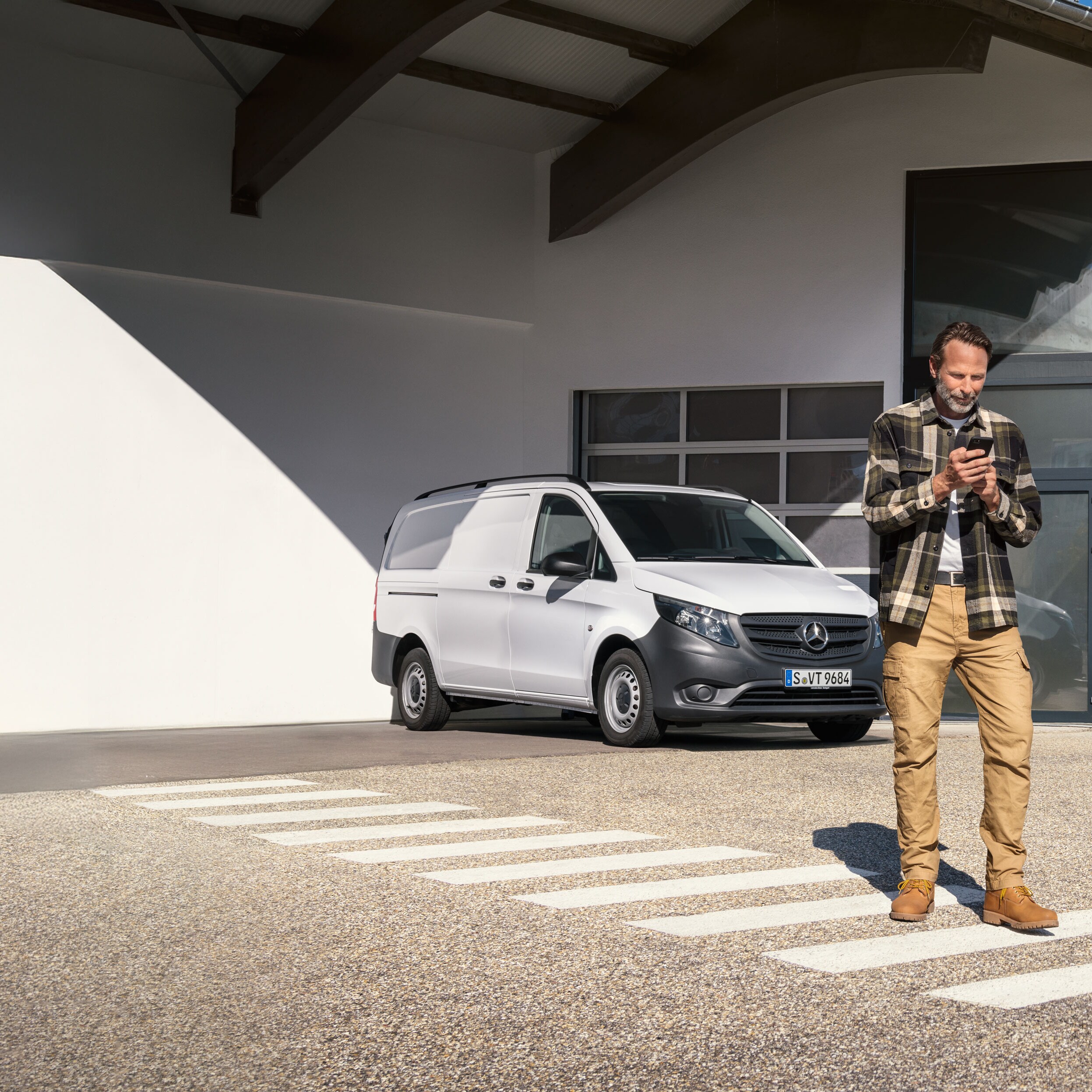 Zákazník si rezervuje termín pomocou svojho mobilného zariadenia, zatiaľ čo stojí pred bielym úžitkovým vozidlom Mercedes-Benz Vito.