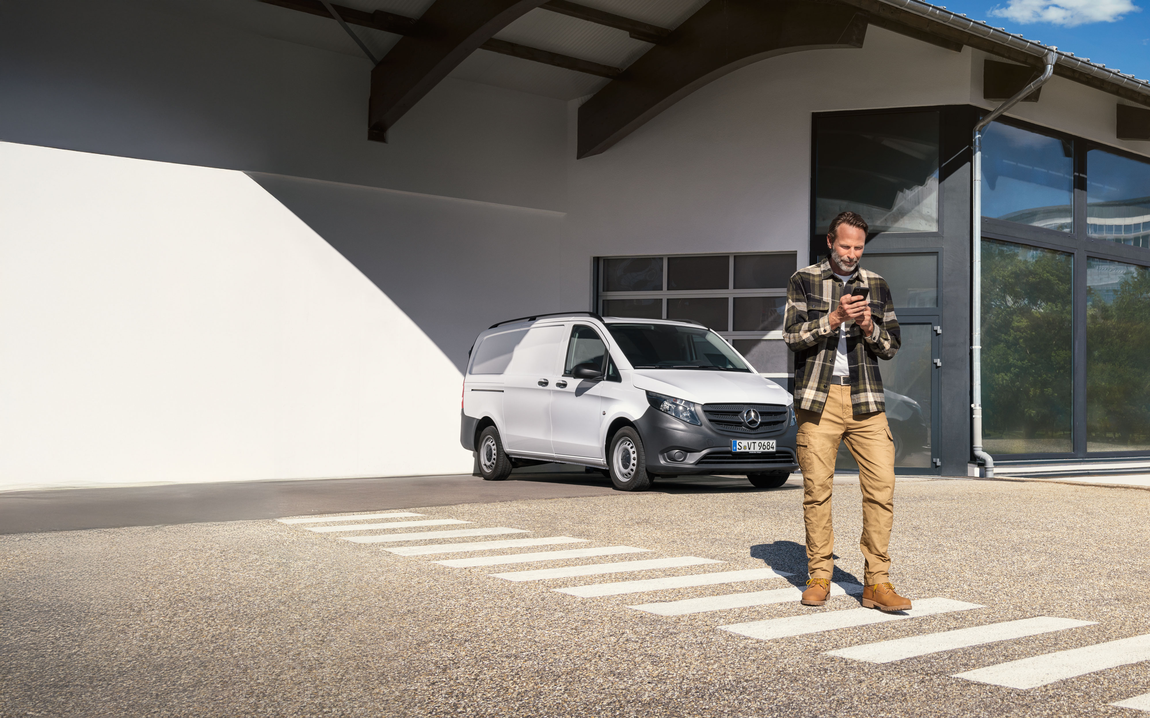 Mercedes-Benz | Údržba | Rezervácia termínu Zákazník si rezervuje termín pomocou svojho mobilného zariadenia, zatiaľ čo stojí pred bielym úžitkovým vozidlom Mercedes-Benz Vito.