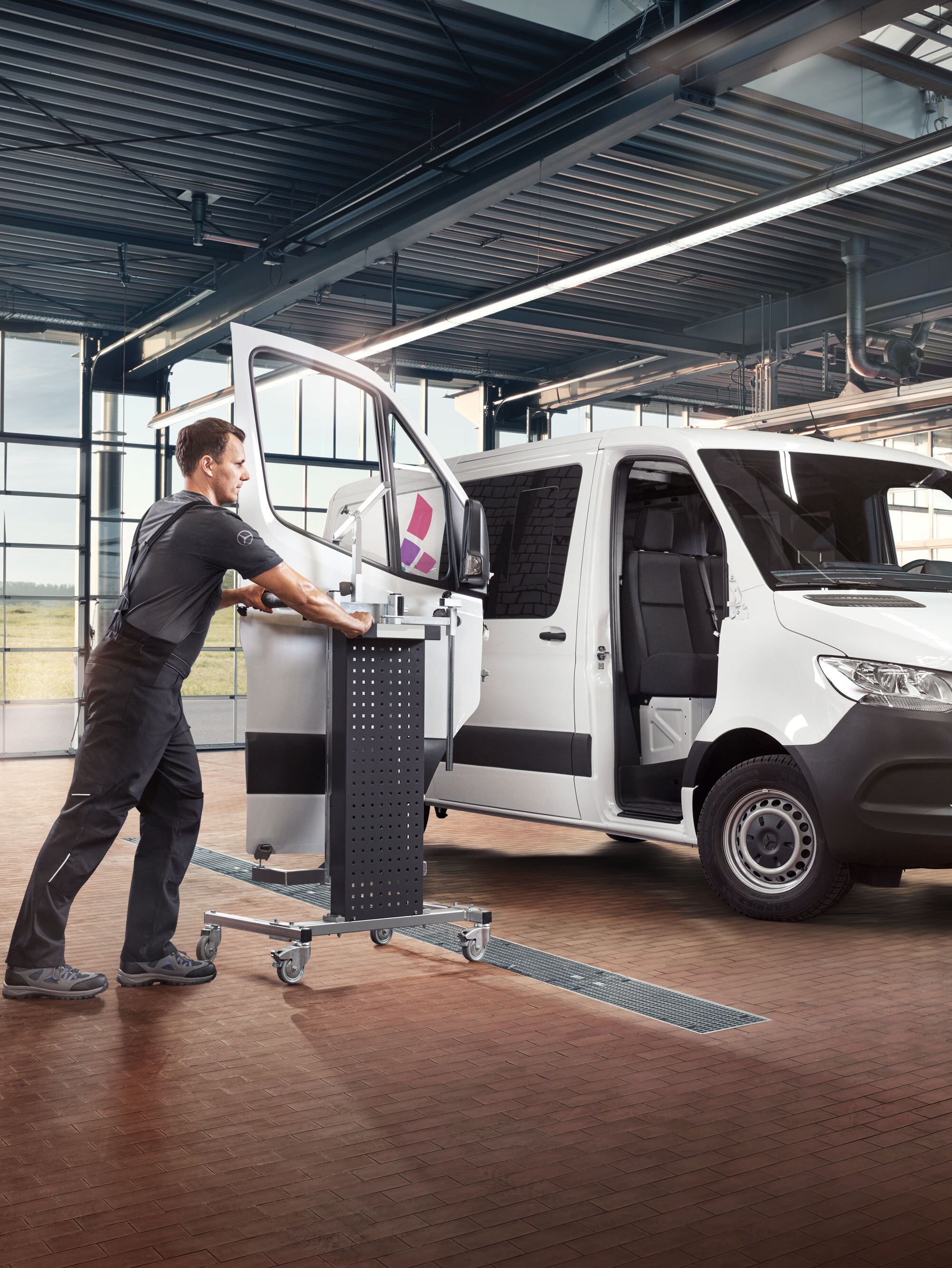 Mechanik montuje dvere na bielom vozidle Mercedes-Benz Sprinter.