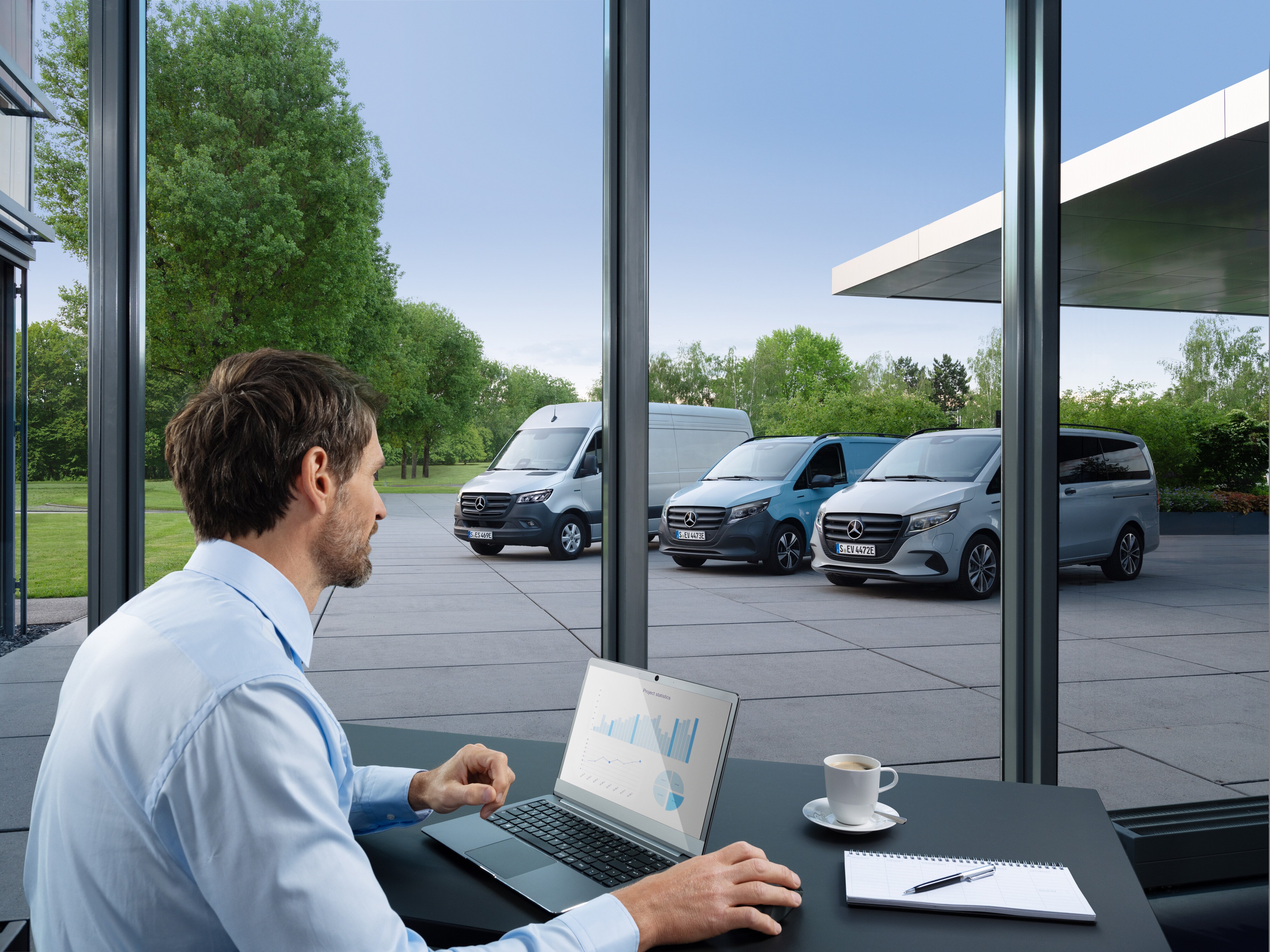 Muž monitoruje niekoľko zaparkovaných úžitkových vozidiel Mercedes-Benz prostredníctvom laptopu, symbol digitálneho manažovania autoparku.